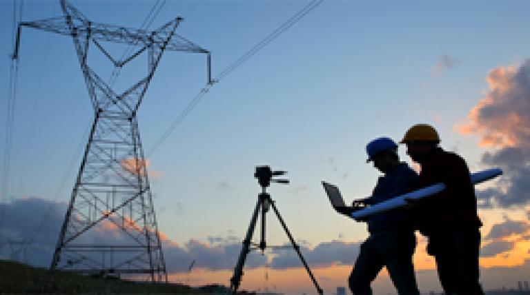 Trabajadores con un portátil junto a una torre eléctrica